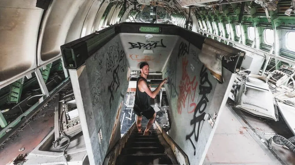 Mężczyzna wchodzi schodami do wnętrza opuszczonego samolotu pokrytego graffiti