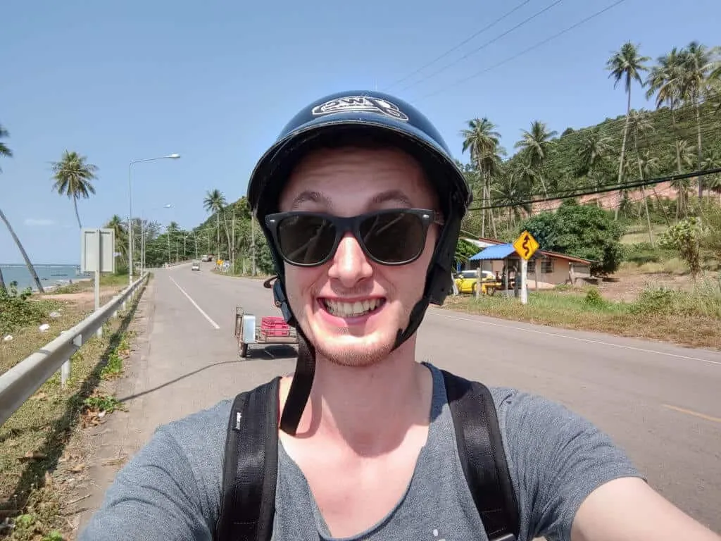 Uśmiechnięty selfie mężczyzny w kasku i okularach na nadmorskiej drodze wśród palm