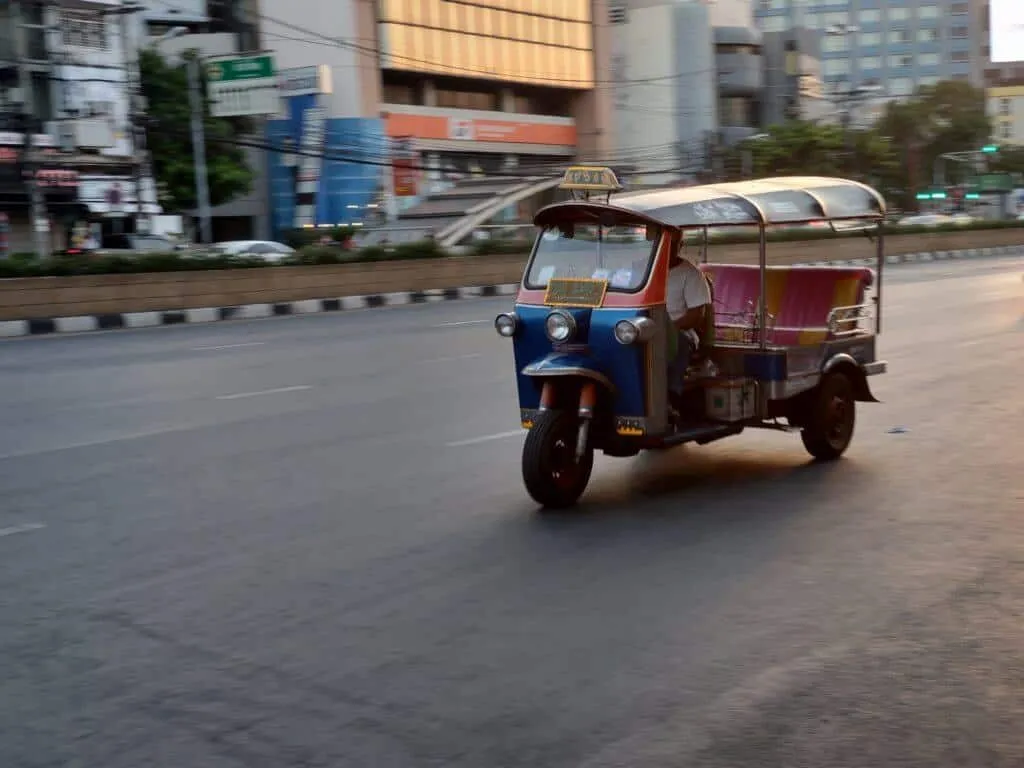 Kolorowy tuk-tuk jadący szeroką ulicą w Bangkoku o zmierzchu, z lekkim rozmyciem ruchu