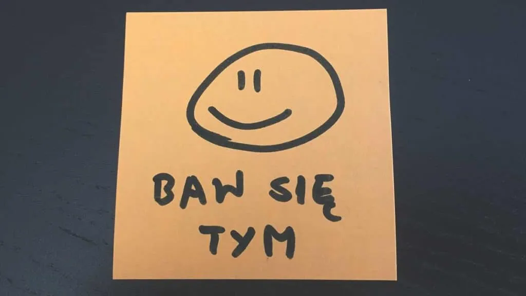 Pomarańczowa karteczka z uśmiechniętą buźką i napisem Baw się tym